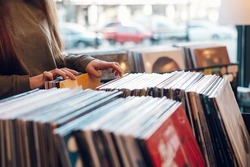 Close shot of a woman hands browsing records in the vinyl record store. Audiophile and music lover. Vintage Vinyl LP In Records Shop.