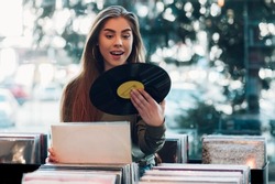 Beautiful young woman holding vinyl while browsing records in a record store. Audiophile and music lover. Vintage Vinyl LP In Records Shop.