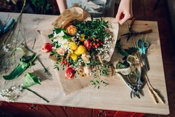 Top view of a woman florist hands making a bouquet while working in a flower shop. Making a bouquet of mixed unusual original flowers. Fresh flowers bouquet arrangement.