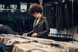 Portrait of a young woman with afro hair selecting records in a vinyl shop. Young audiophile hipster woman in a record store. Fashionable and stylish.