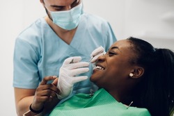 Beautiful black young woman sitting in medical chair while dentist fixing her teeth at dental clinic. Regular check-ups at the dentist. Healthy smile concept.
