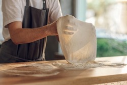 Skilled chef preparing dough for pizza rolling with hands while working in a pizza place. The process of making pizza.Focus on a man hands.