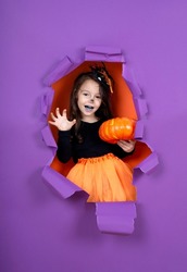 Happy child girl in witch costume to halloween, purple background
