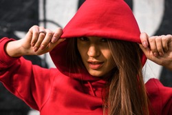 Close up portrait of Adorable caucasian girl in costume for sport. Beautiful young fit fitness sport model in red hoodie near the painted wall.