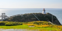 A seascape of the lighthouse on Cape Enrage, New Brunswick, Canada, on the rocky hill with the wooden walkway and fences creating angles