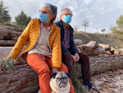 
Nice adult couple outdoors in winter clothes and with mask walking in the woods with their pug dog