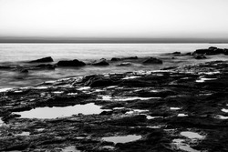 Black and white long exposure of a sunrise right next to a huge lake, with armour stone for erosion control as foreground. 
