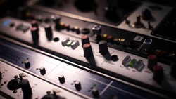 Recording gears in a music production studio. Low light, high contrast. Smooth and silk feeling. Focus on some knobs and buttons to get the depth of sound with the shallow depth of field.