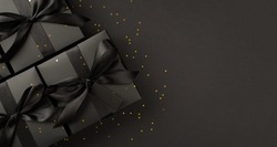 Top view photo of black gift boxes with black ribbon bow tag and golden confetti on isolated black background with blank space