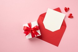 Top view photo of saint valentine's day decorations small hearts white giftbox with red bow open red envelope with paper card on isolated pastel pink background with empty space