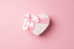 Top view photo of valentine's day decorations heart shaped giftbox with pink ribbon bow on isolated pastel pink background with copyspace