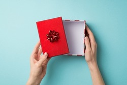 First person top view photo of valentine's day decorations woman's hands opening giftbox with red lid and star bow on isolated pastel blue background with empty space