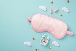Top view photo of pink satin sleeping mask alarm clock earplugs clouds and golden stars on isolated pastel blue background with copyspace