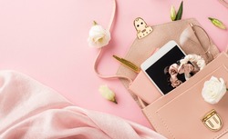 Top view photo of woman's day composition soft textile open pink leather bag with mobile phone scrunchies glasses pen and prairie gentian flower buds on isolated pastel pink background with copyspace