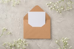 Top view photo of woman's day composition open craft paper envelope with paper card and white gypsophila flowers on isolated textured grey concrete background with empty space