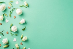 Top view photo of an big white eustomas green flower buds and leaves with white and brown confetti in shape of hearts in the left side of the pastel turquoise isolate background empty space
