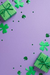 Top view vertical photo of st patricks day decorations shamrocks two green gift boxes and clover shaped confetti on isolated pastel lilac background with copyspace