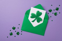 Top view photo of st patricks day decor trefoil shaped confetti green envelope with paper sheet and shamrock on isolated pastel violet background