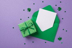 Top view photo of saint patricks day decor clover shaped confetti green envelope with letter and green giftbox with polka dot pattern on isolated pastel lilac background with empty space