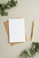 Business concept. Top view vertical photo of paper card craft paper envelope gold pen and eucalyptus on pastel grey background with blank space
