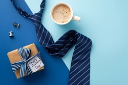 Father's Day concept. Top view photo of craft paper giftbox with silk ribbon bow and postcard blue tie cup of coffee and cufflinks on bicolor blue background