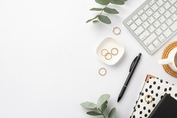 Business concept. Top view photo of workstation keyboard black and white stationery trendy planners pen cup of coffee on rattan placemat gold rings and green eucalyptus on isolated white background
