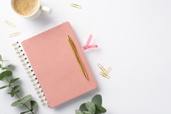 Business concept. Top view photo of workplace pink notepad with tab gold pen cup of coffee clips and eucalyptus on isolated white background
