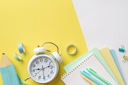 Back to school concept. Top view photo of school supplies alarm clock colorful notebooks pencil-case pens binder clips and adhesive tape on bicolor yellow and white background