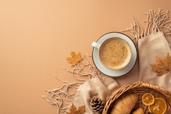 Autumn aesthetic concept. Top view photo of cup of hot drinking on saucer wicker tray with croissants dried orange slices autumn maple leaves scarf and pine cones on isolated beige background