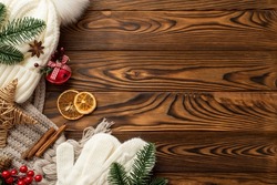Winter holidays concept. Top view photo of headwear scarf mittens jingle bell pine branches wicker star dried orange slices mistletoe berries cinnamon sticks on wooden desk background with copyspace