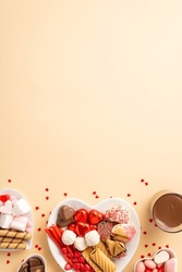 Valentine's Day concept. Top view vertical photo of heart shaped dishes with sweets cookies candies glass of drinking and confetti on isolated beige background with empty space