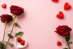 Valentine's Day concept. Top view photo of red roses heart shaped candles and saucer with chocolate candies on isolated pastel pink background with copyspace