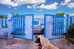 Man used hand remote control to open swing gate door by motor automation is home security system with blue cloud sky background.