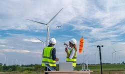 Engineers using meteorological and drone instrument collect data laptop to measure the wind speed, temperature,humidity and solar cell system on wind turbine station is sustainable energy concept.
