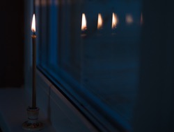 A burning candle is reflected in the window late at night. Easter at home. Lighting a candle on Easter night, a stay-at-home promotion on public holidays. Family time.