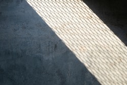 Light spilled through the steel wire of railings or baluster.Saw a shadow on raw concrete floor like net texture to strip of shadow on cement.