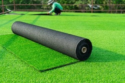 Roll of an artificial turf laying background. A synthenic grass layer. Greenering of the yard of , green lawn background with workers pave the counterfeit grass.