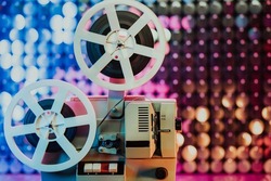 Retro reel with film rotating on sequins kinetic wall, colorful light. Old-fashioned 8mm projector playing in decorated room. Vintage movie objects, cinema, Hollywood concept