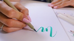 Calligrapher hands writes word on white paper. Inscribing ornamental decorated letters. Calligraphy, graphic design, lettering, handwriting, creation concept. 