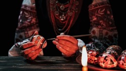 Ukrainian woman painting traditional ornamets on Easter egg - pysanka. Artist working in national costume under candle light. Preparation for Christian holiday. High quality 