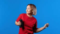 Woman listening music by wireless portable speaker - modern sound system. Young girl dancing, enjoying on blue studio background. She moves to rhythm of music. High quality photo