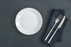 Empty white plate on black table and napkin. Food background for menu, recipe. Table setting. Flatlay, top view. Mockup for restaurant dish