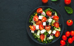 Greek salad with tomato and fresh vegetables in white bowl on dark background. Top view