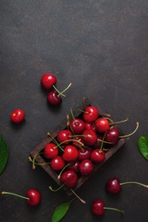 Cherry with leaf water drops on wooden box on dark brown stone table. Ripe ripe cherries. Sweet red cherries. Top view. Rustic style. Fruit Background
