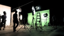 Behind the scenes of TV commercial movie film or video shooting production which crew team and camera man setting up green screen for chroma key technique in big studio.