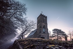 Wide angle shot of a misty church and gravestones on an atmospheric cold winter morning at sunrise.