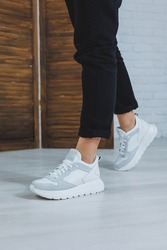 Beautiful women's shoes with legs, leather white sneakers, in the interior of a room or office, shoes for a woman, black trousers and white sneakers, casual and modern style, modern and trendy