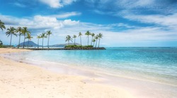 A beautiful beach scene in the Kahala area of Honolulu, with fine white sand, shallow turquoise water, a view of coconut palm trees and Koko Head in the background.