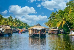 In the Kerala Backwaters of southern India, covered barges travel along a narrow canal lined with coconut palm trees, part of a large network of interconnected inland waterways.
