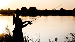 Silhouette of a young girl with a fishing rod on the river Bank.